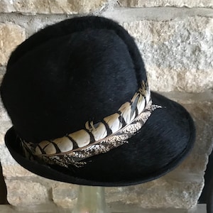 May include: A black fedora hat with a pheasant feather band.