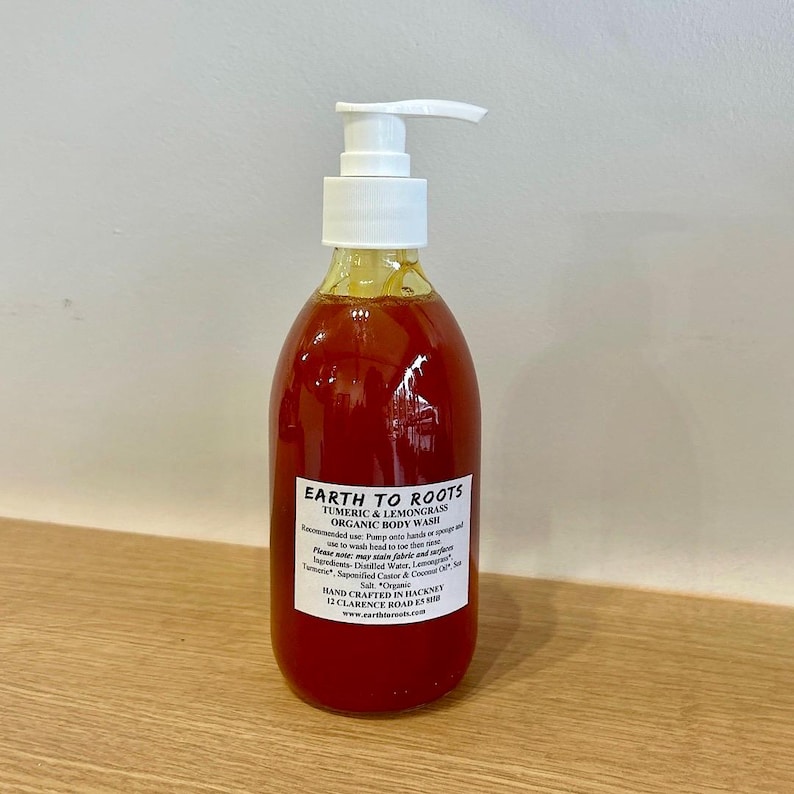 May include: A clear bottle with a pump dispenser filled with a bright orange liquid. The bottle is labeled "EARTH TO ROOTS TUMERIC & LEMONGRASS ORGANIC BODY WASH". The label also includes the ingredients and instructions for use.