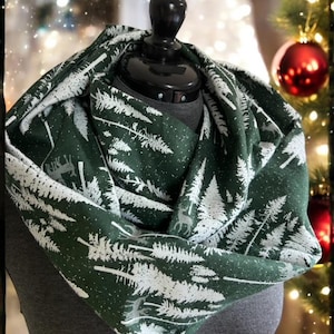 May include: A green infinity scarf with a white print of pine trees and deer. The scarf is made of a soft, comfortable fabric and is perfect for keeping warm in the winter.