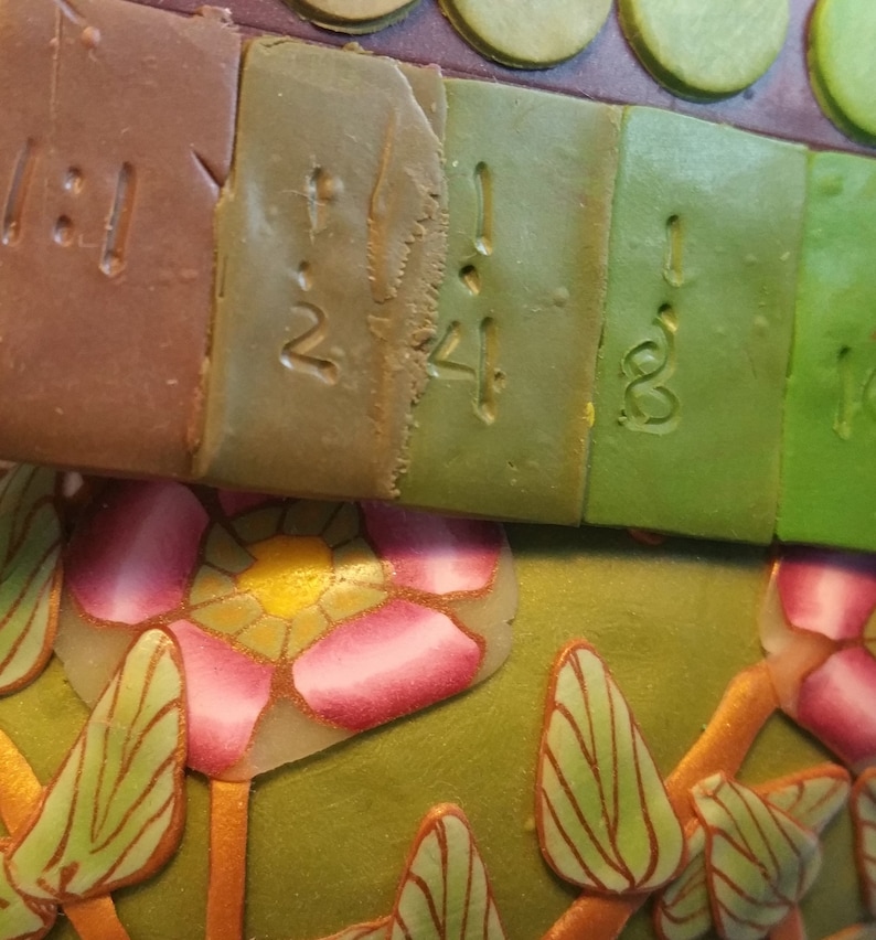 May include: Close-up of a set of polymer clay squares with numbers 12, 24, 18, and 1 written on them. The squares are arranged in a row and are different shades of green and brown.