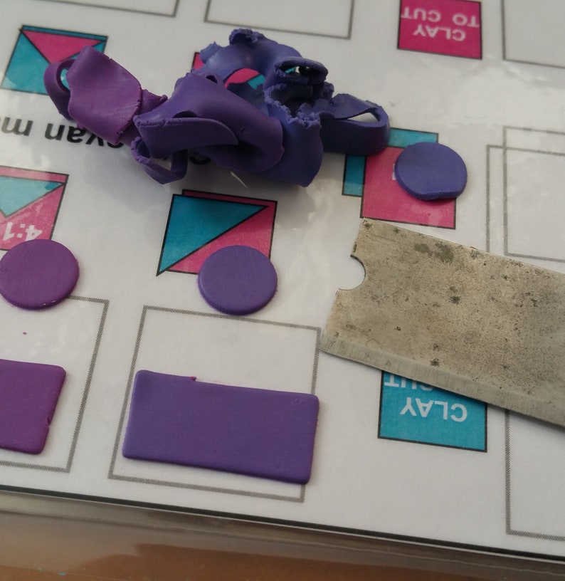 May include: Purple modeling clay on a white surface with a metal clay tool and a printed sheet with the words "CLAY TO CUT" and "CLAY CUT".