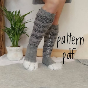 May include: Knee-high grey and black striped knitted leg warmers with white fluffy paw-like feet. The leg warmers are displayed on a light grey surface. The text "pattern pdf" is written in black cursive on the right side of the image.