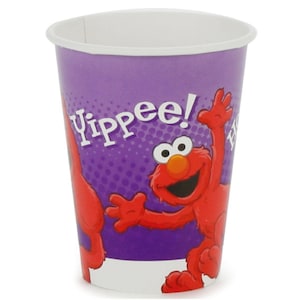 May include: A purple paper cup featuring a graphic of the red character Elmo with the text Yippee! printed in white. The cup has a white rim and a white base, with a dotted pattern background behind the character and the printed word.