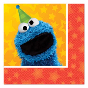 May include: A square paper napkin featuring a blue, furry monster character with large white eyes and a black mouth. The character wears a green party hat with a blue pom-pom. The background is bright yellow with orange star patterns.