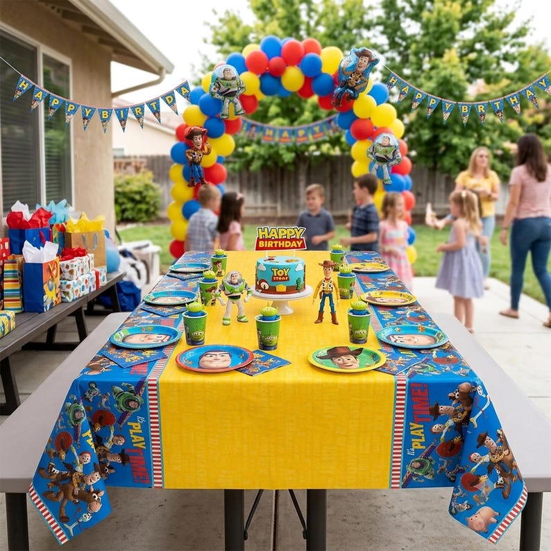 May include: A Toy Story themed birthday party setup featuring a yellow and blue tablecloth with character prints, matching plates, cups, and a central cake. An arch of red, yellow, and blue balloons stands behind the table with a Happy Birthday banner.