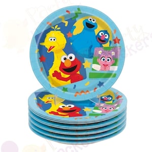 May include: A stack of round light blue paper plates featuring Sesame Street characters including Big Bird, Elmo, Cookie Monster, Grover, and Abby Cadabby. The design includes colorful confetti shapes like stars and squiggles scattered across the surface.