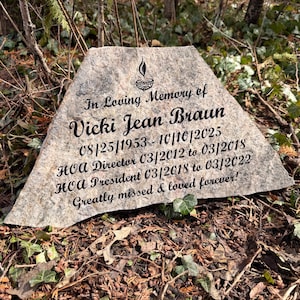 May include: A memorial stone with the inscription "In Loving Memory of Vicki Jean Braun" and dates 08/25/1953-10/10/2025. The stone also lists her roles as HOA Director and President, with the phrase "Greatly missed & loved forever!"