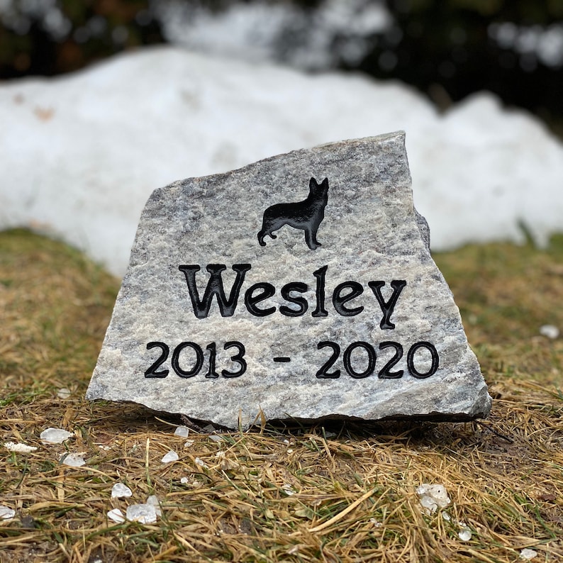 May include: A gray granite stone engraved with a black silhouette of a dog, the name "Wesley", and the dates "2013 - 2020".