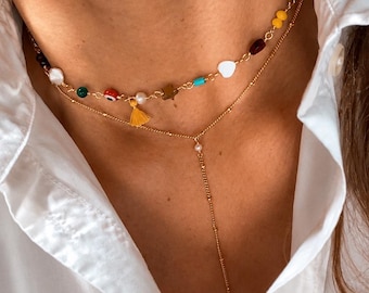 May include: A layered gold-tone necklace set featuring a choker with multicoloured beads, including a small yellow tassel, a white heart, and an evil eye charm, paired with a delicate Y-shaped chain necklace with a single pearl and a bar toggle.