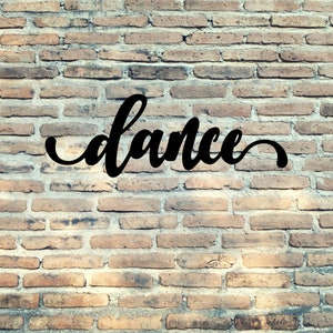 May include: The word "dance" written in black cursive script on a brick wall.