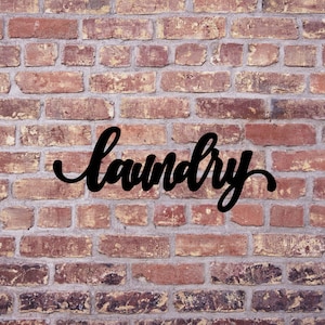 May include: Black metal sign with the word "laundry" in a cursive font, mounted on a brick wall.