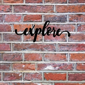 May include: The word "explore" written in black cursive font on a red brick wall.