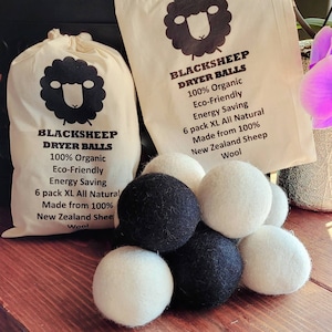 May include: Six black and white wool dryer balls in a pile on a wooden surface. The dryer balls are made from 100% New Zealand sheep wool. The balls are packaged in a white bag with a black sheep logo and the text "BLACKSHEEP DRYER BALLS 100% Organic Eco-Friendly Energy Saving 6 pack XL All Natural Made from 100% New Zealand Sheep Wool".