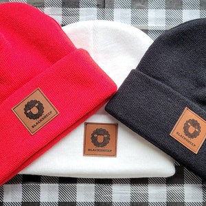 May include: Three knit beanies in red, white, and black with a brown leather patch featuring a black sheep silhouette and the text "BLACKSHEEP".