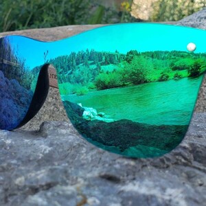 May include: A pair of sunglasses with a wooden frame and green mirrored lenses. The sunglasses are resting on a gray rock.