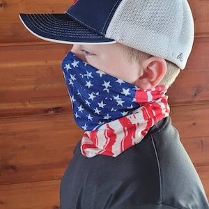 May include: A young person wearing a black and white baseball cap with a red, white, and blue patterned face covering. The face covering has a design resembling the American flag.