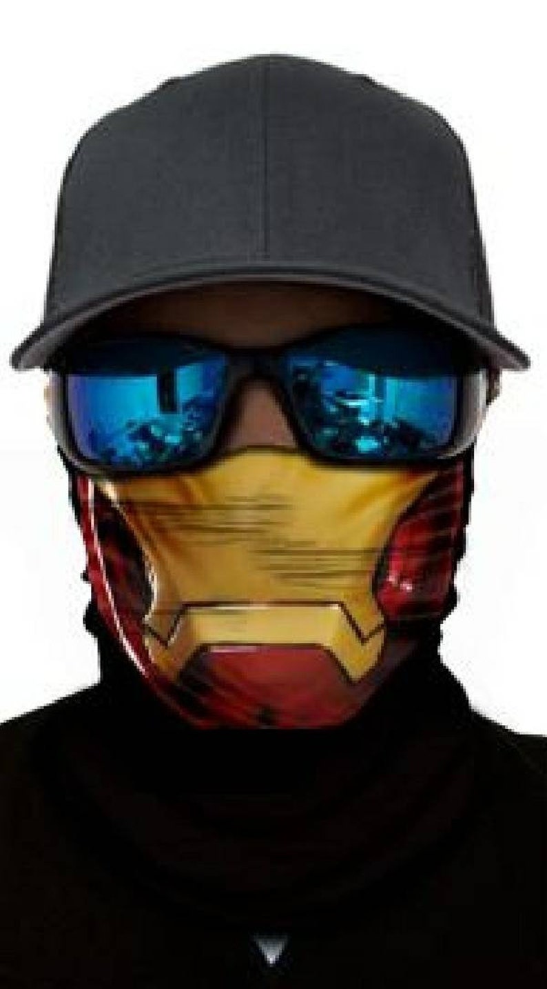 May include: A black baseball cap with a red and yellow face mask featuring a superhero design. The face mask has a yellow and red design with a metallic sheen.