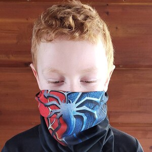 May include: A young person wearing a black shirt with a red and blue patterned neck gaiter. The gaiter features a spider web design.