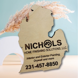 May include: A wooden cutout of the state of Michigan with the text "NICHOLS HOME FINISHING SOLUTIONS, LLC." and the phone number "231-457-8850" engraved on it. The text also includes "Interior and Exterior Painting, Drywall and more".