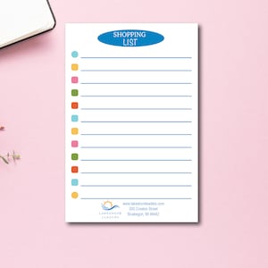 May include: A white shopping list notepad with a blue oval that says "SHOPPING LIST" at the top. The notepad has colorful dots and blue lines for writing. The bottom has a logo and website address.