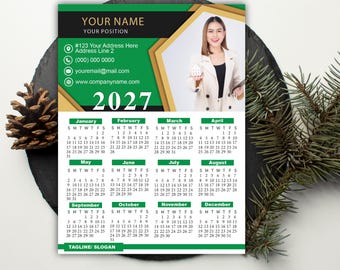 May include: A 2027 wall calendar template featuring a green and gold color scheme. The design includes a placeholder for a name, position, contact details, and a photo of a person holding a small house model. The calendar displays all twelve months.