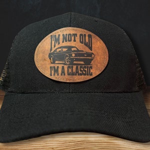 May include: Black trucker hat with a brown leather patch that says "I'm not old, I'm a classic" with a vintage car graphic.