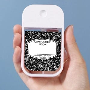 May include: A white, rectangular hand sanitizer spray bottle with a black and white composition book design. The composition book label reads "COMPOSITION BOOK" with details about the number of sheets and pages. The bottle is held against a light blue background.