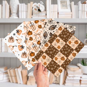 May include: Four sheets of patterned paper with fall-themed designs. The patterns include pumpkins, footballs, leaves, and coffee drinks in shades of orange, brown, and cream. The papers are held in a hand against a backdrop of books and decorative items.