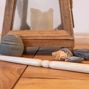 以下が含まれることがあります： 丸みを帯びた端を持つ木製の棒が、石と貝殻が置かれた木製の床の上に置かれています