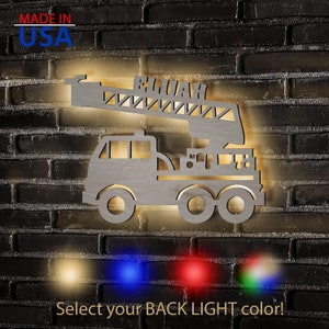 May include: A wooden fire truck night light with the name "ELIJAH" on the ladder. The light is illuminated with a warm white glow. The image shows four color options for the back light: yellow, blue, red, and green.