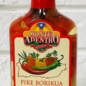 Puede incluir: Una botella de vidrio de salsa picante Monte Adentro Pike Borikua. La botella está llena de pimientos rojos y amarillos y tiene una tapa roja. La etiqueta es blanca con texto negro y una estrella roja. La etiqueta dice "Monte Adentro Hot Sauce" y "Pike Borikua hot sauce". La etiqueta también dice "Puerto Rico Artisan Gourmet Sauce", "100% Natural", "Sin azúcar añadido", "Agitar bien", "Peso neto 6,7 oz" y "200 ml".
