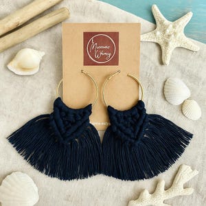 May include: A pair of black macrame earrings with gold hoops. The earrings have a fringe design and are handmade.