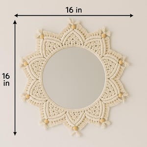 May include: A round mirror with a cream-colored macrame sunburst design. The mirror is 16 inches in diameter and features wooden bead accents.