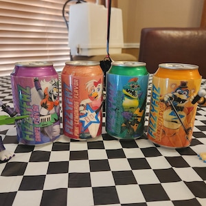 Könnte beinhalten: Vier bunte Dosen Fizz Faz-Soda mit verschiedenen Geschmacksrichtungen: Traube, rosa Limonade, blauer Himbeer und Orange. Jede Dose zeigt einen anderen Comic-Charakter aus der Fazbear-Band.