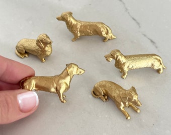 May include: Five gold dachshund figurines, each with a different pose. The figurines are made of a shiny, metallic gold material.