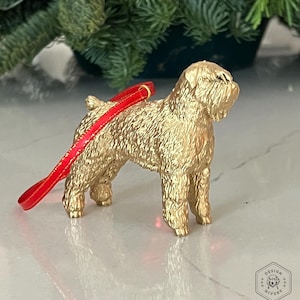 May include: Gold-colored ornament of a dog with a red ribbon attached. The dog is standing on a white surface.