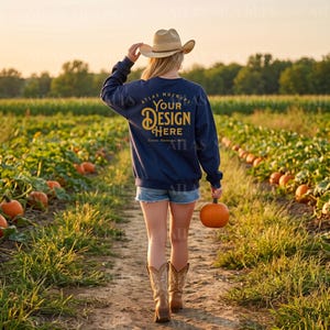 May include: A navy blue long-sleeve sweatshirt with the gold text "YOUR DESIGN HERE" on the back, worn with denim shorts, a tan cowboy hat, and brown leather boots. The sweatshirt features a crew neckline and a relaxed fit, shown from behind.