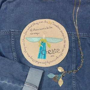 May include: A denim jacket with a round embroidered patch featuring an angel with wings and the text "Create one thing you love, for what they are, they see them for what they can be Creative people do not see things merely for what they can be. If there seems to be no way..."