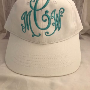 May include: White baseball cap with a teal embroidered monogram of the letters "C.S.W."