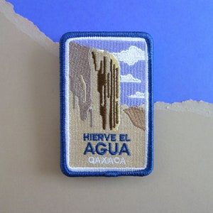 May include: A blue and beige embroidered patch with a depiction of a rock formation and the text "Hierve el Agua Oaxaca".