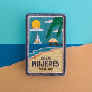 May include: Embroidered patch featuring a beach scene with a yellow sun, sailboat, and palm tree. The text "ISLA MUJERES MEXICO" is displayed in a tan rectangle with a blue border. The background is blue and tan.