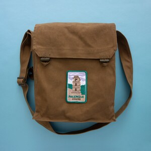 May include: A brown canvas messenger bag with a green and white embroidered patch that says "Palenque Chiapas".