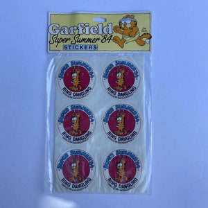 May include: A pack of six Garfield Super Summer '84 stickers. Each sticker features Garfield in a red circle with the text "Super Summer '84" and "Ring Dangling".