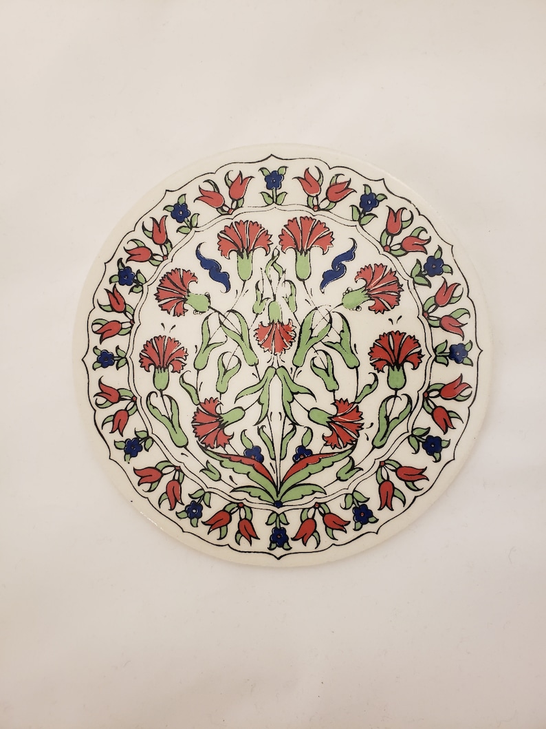 May include: A white ceramic plate with a red, green, and blue floral design. The design features stylized carnations and tulips.