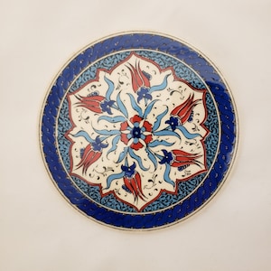 May include: A round ceramic plate with a blue and white border and a floral design in the center. The design features red, white, and blue tulips and leaves.
