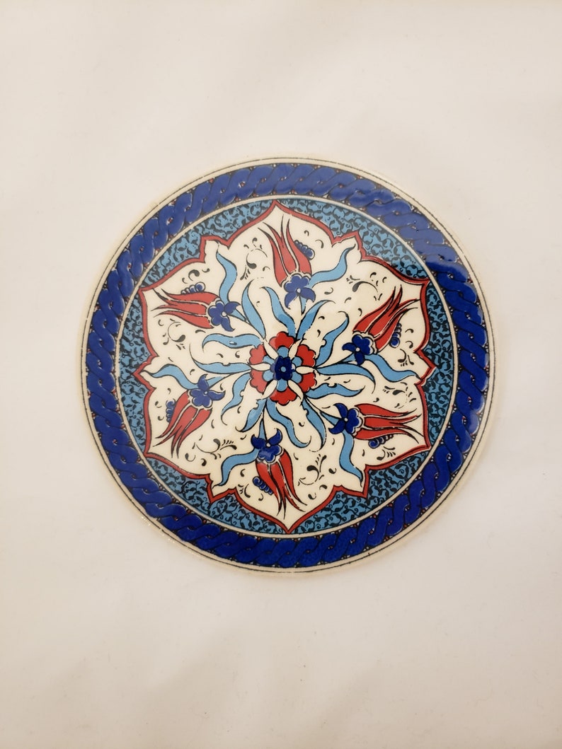 May include: A round ceramic plate with a blue and white border and a floral design in the center. The design features red, white, and blue tulips and leaves.