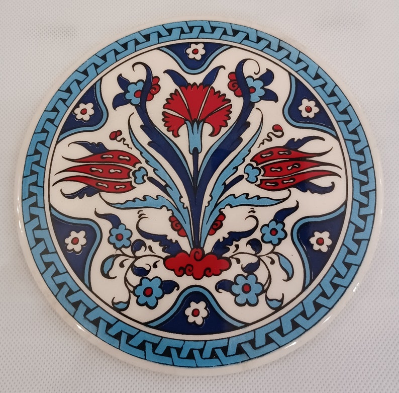 May include: A round ceramic coaster with a blue and white border and a floral design in the center. The flowers are red, blue, and white.