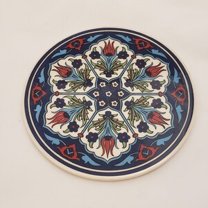 May include: A round ceramic coaster with a blue, white, and red floral design. The design features stylized tulips and leaves.