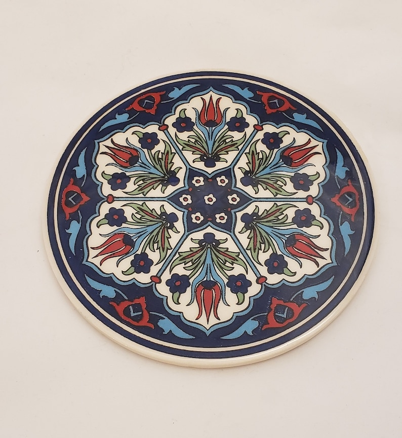 May include: A round ceramic coaster with a blue, white, and red floral design. The design features stylized tulips and leaves.
