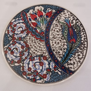 May include: A round ceramic coaster with a blue, white, and red floral pattern. The design features stylized flowers and leaves with intricate details.